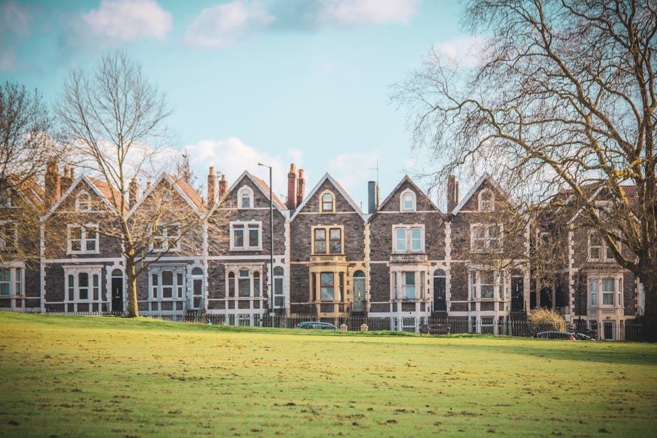 A row of semi-detached houses with brick and white rendered exteriors, situated along a residential street on a cloudy day. Each property features large bay windows with white frames, some with decora